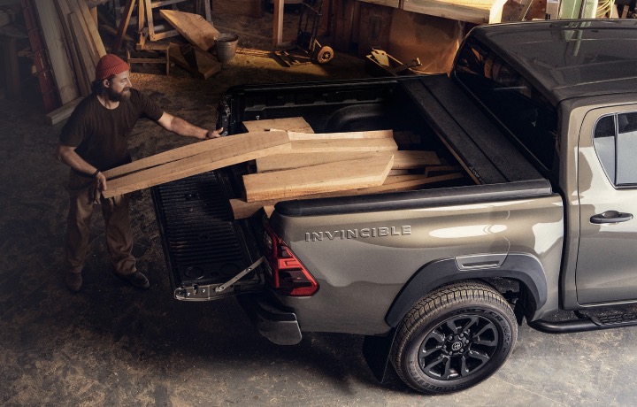 Eine Person in einer Werkstatt entlädt Holzscheite von der Ladefläche eines Toyota Hilux Pick-up Truck