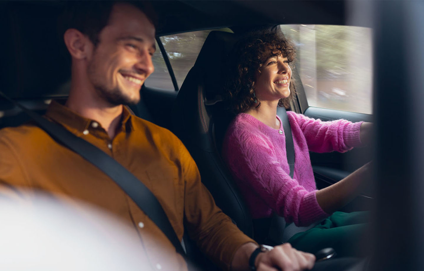 Innenraum eines Autos in dem zwei Personen sitzen und lächeln