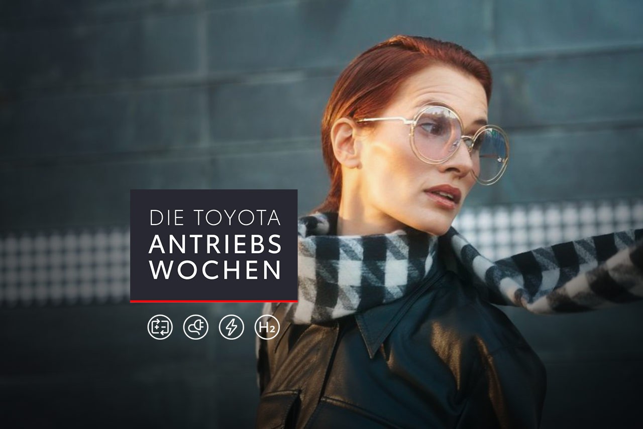 Frau mit Brille und Schal schaut über ihre Schulter, auf dem Bild ein Störer mit Die Toyota Antriebswochen