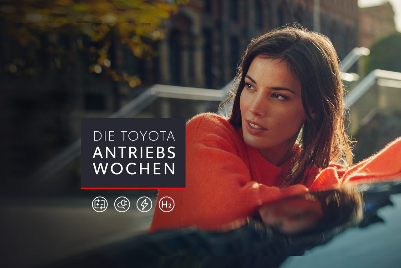 Frau mit Brille und Schal schaut über ihre Schulter, auf dem Bild ein Störer mit Die Toyota Antriebswochen