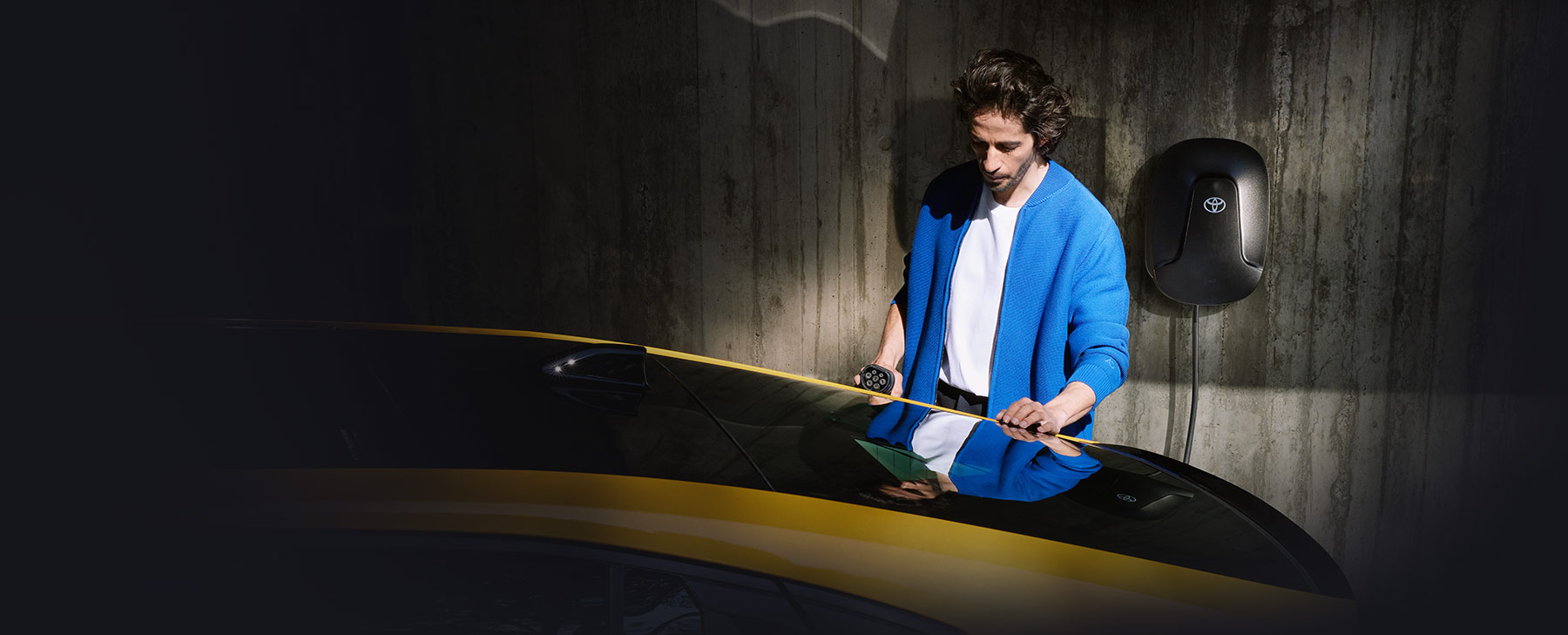 Mann in blauer Jacke hält Ladekabel einer Wallbox in der Hand und schließt es an sein Auto an