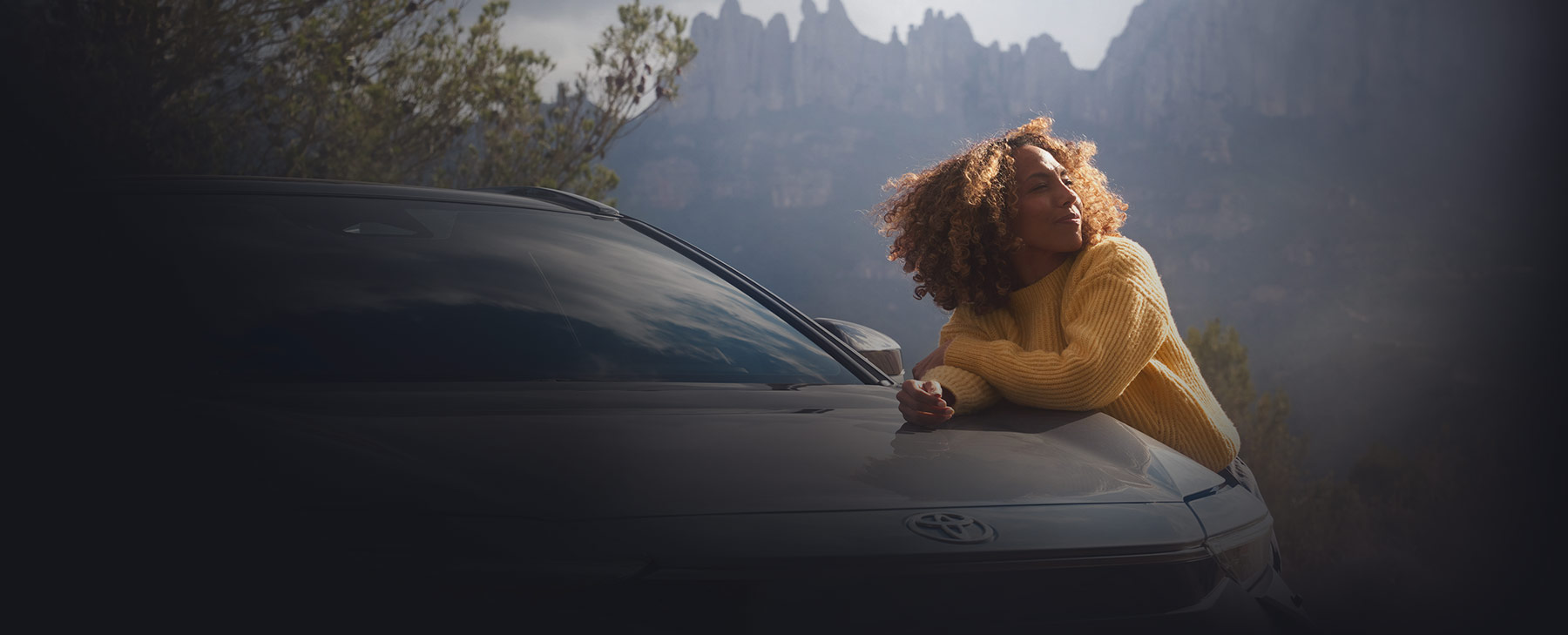 Frau mit lockigen Haaren stützt sich auf einem Toyota-Modell ab