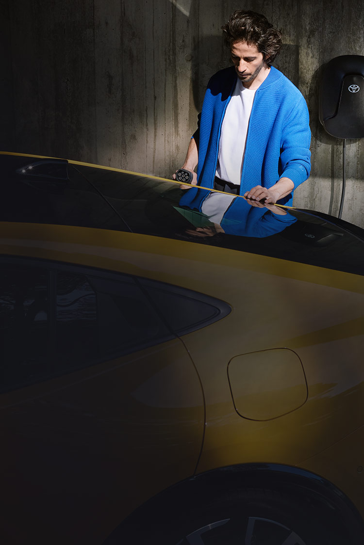 Mann in blauer Jacke hält Ladekabel einer Wallbox in der Hand und schließt es an sein Auto an