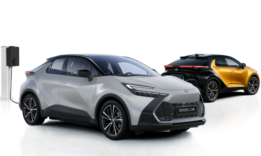 Ein silberner Toyota C-HR steht neben einer Ladesäule, dahinter steht ein schwarz-orangener Toyota C-HR