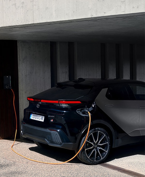 Silberner Toyota C-HR steht neben einer Ladesäule vor einer modernen abstrakt geformten orangenen Wand