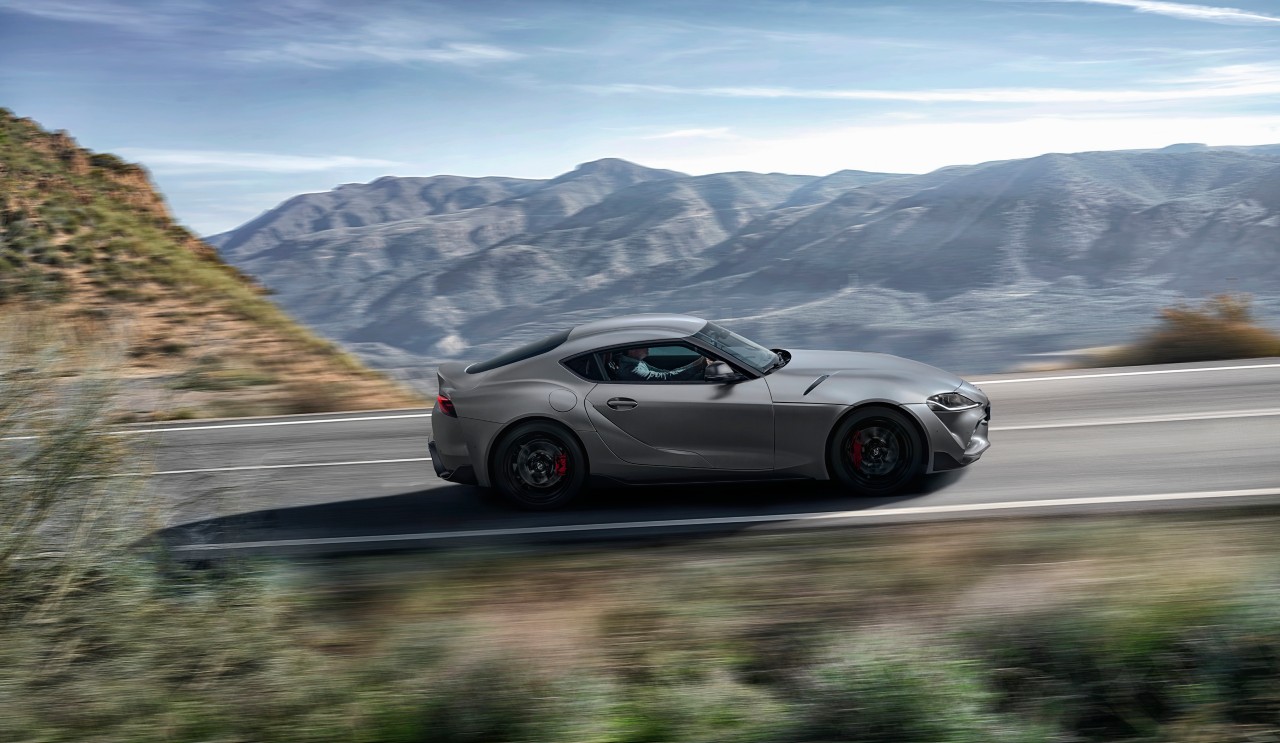 Ein grauer GR Supra fährt auf einer Landstraße mit Blick auf eine mediterrane Bergebene..