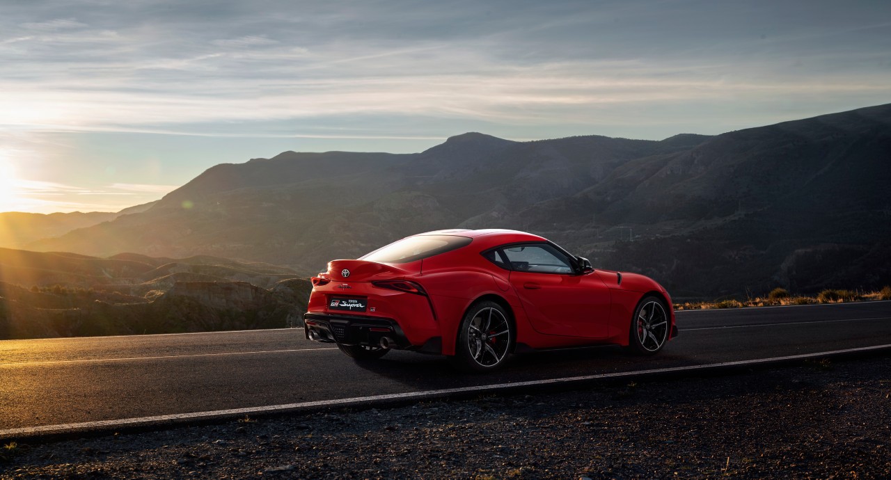 Ein roter Toyota Supra auf einer Landstraße. Im Hintergrund Berge.