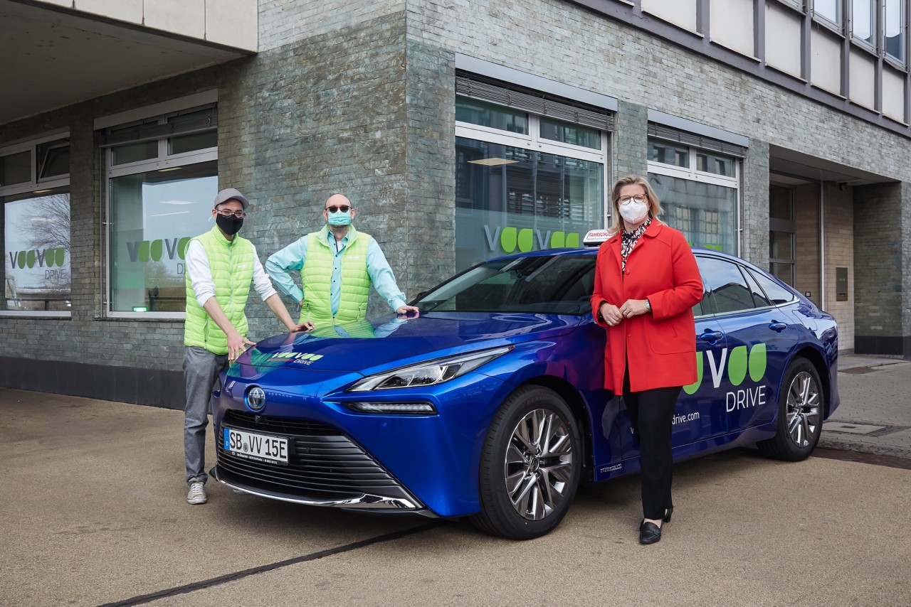 Drei Personen und ein blauer Toyota Mirai