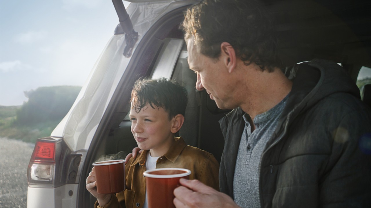 Eine Familie sitzt im Gepäckraum eines Toyota und trinkt Kaffee