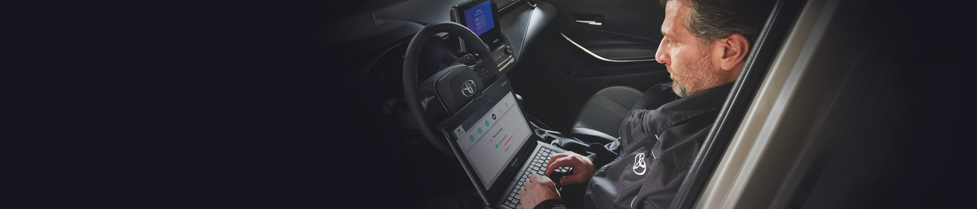 Toyota-Mechaniker sitzt in einem Auto und prüft es mit einem Laptop