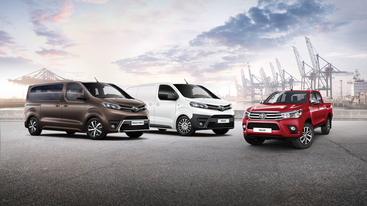 Ein brauner Proace Verso, ein weißer Proace und ein roter Hilux. Im Hintergrund Hafenkräne.
