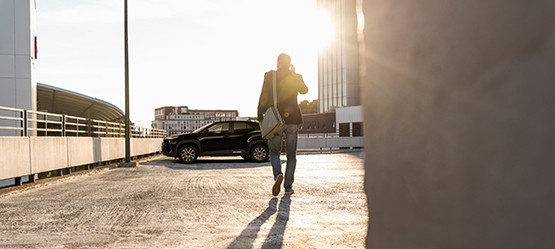 Auf einem Parkdeck geht ein Mann mit Handy am Ohr und weißer Tasche der Sonne entgegen zu seinem geparkten Toyota Fahrzeug.