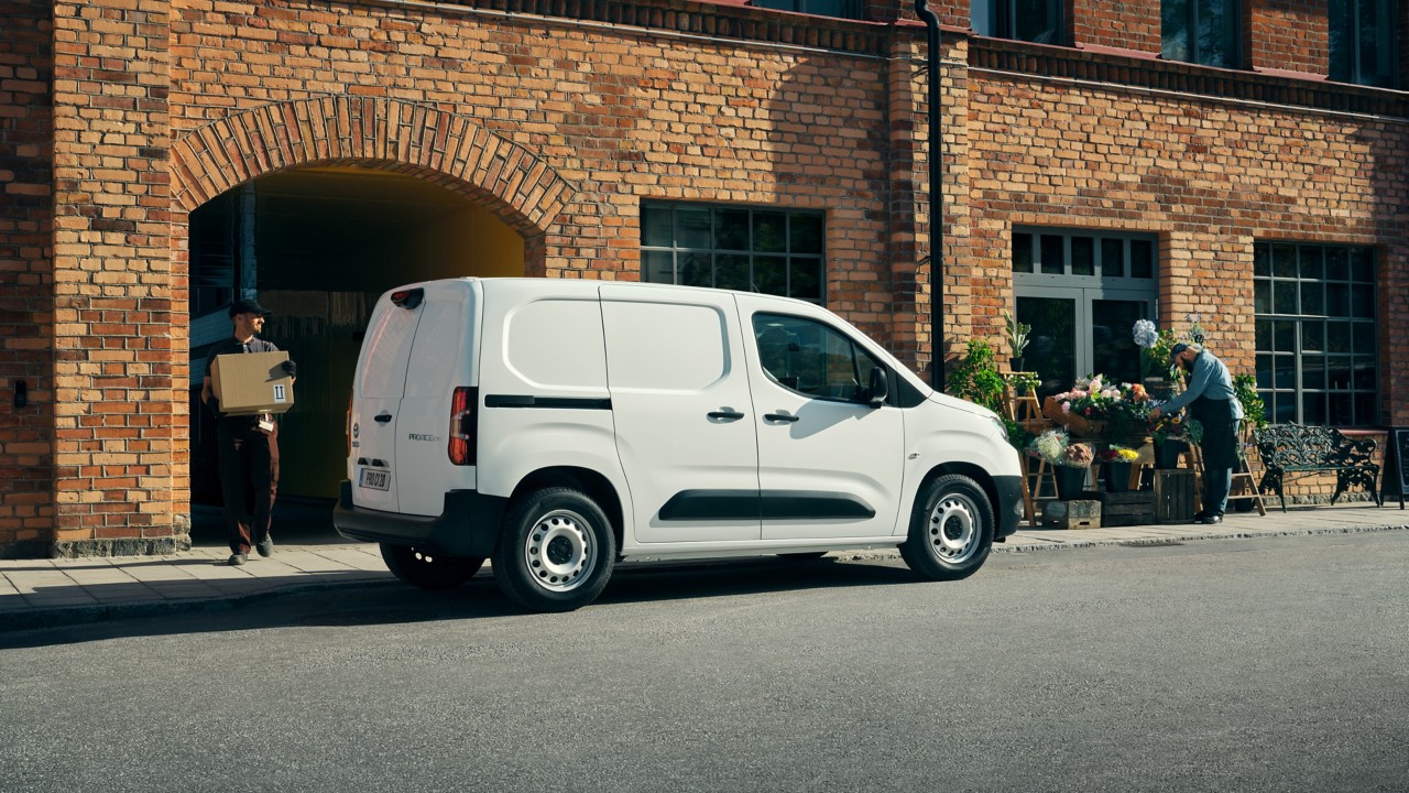 Ein weißer Proace City Electric steht vor einem Ladengeschäft, aus dem ein Paketbote herauskommt.