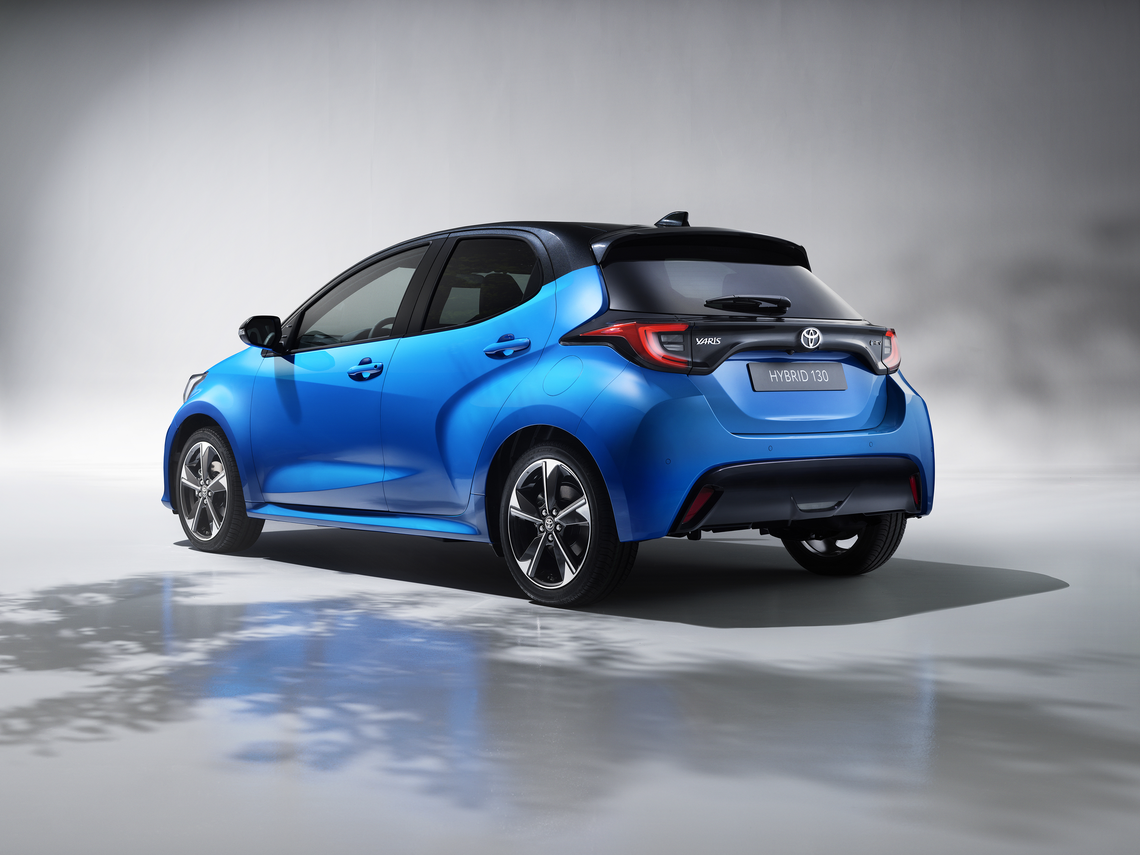 Ein blauer Toyota Yaris von der Seite vor einem grauen Hintergrund mit Schatten von Bäumen