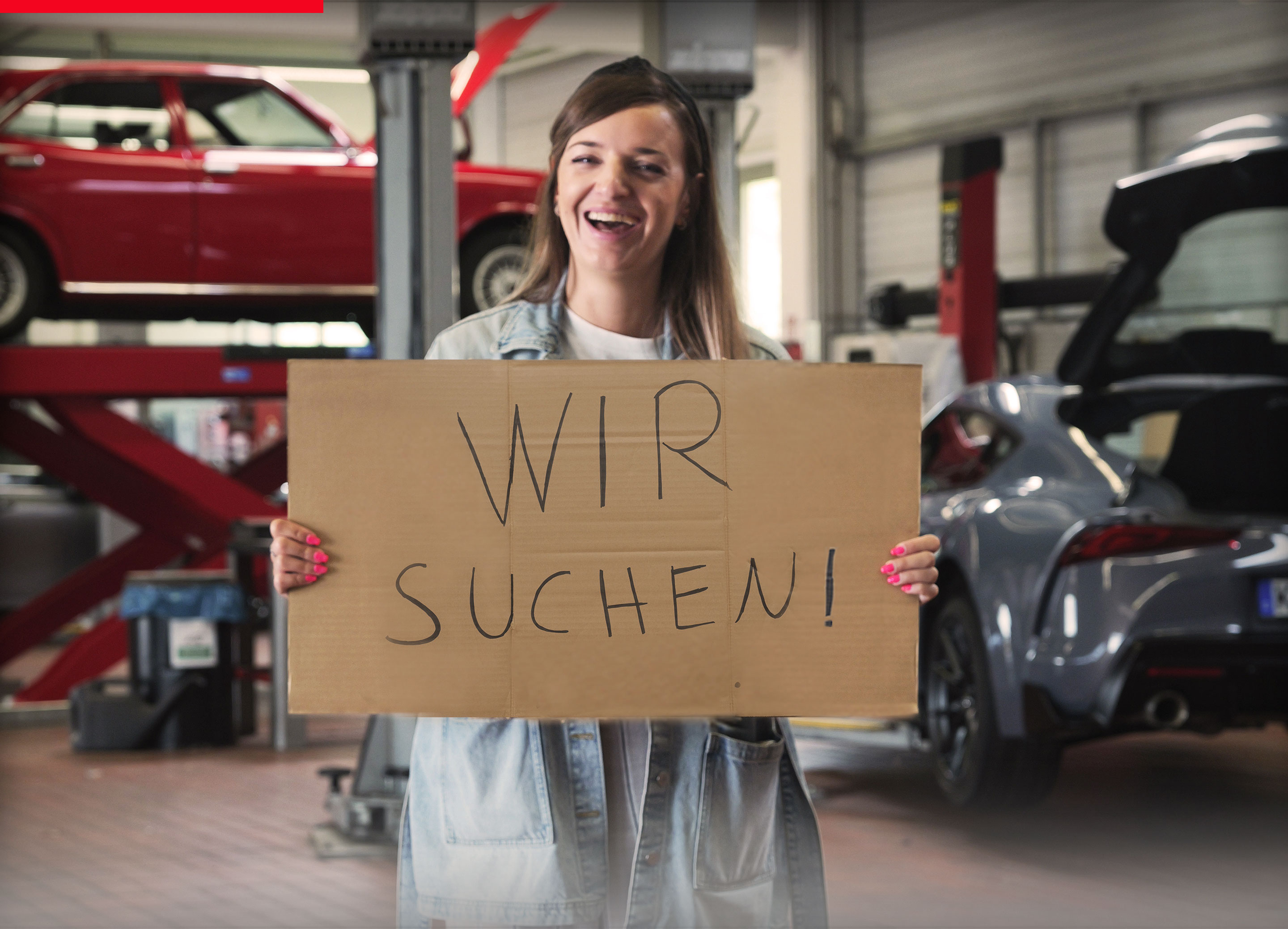 Azubi mit Schild in der Hand steht in einer Werkstatt: Wir suchen dich