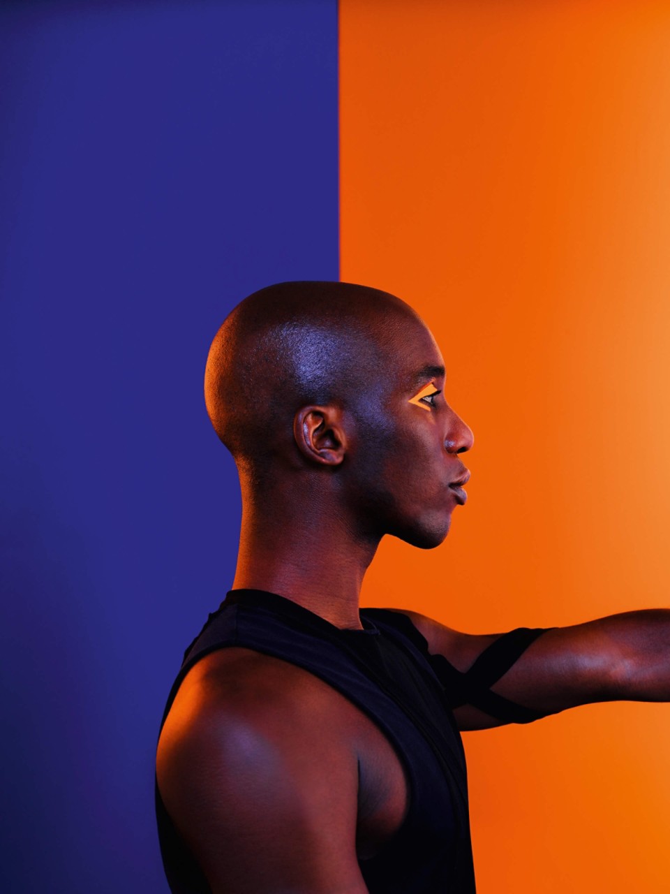 Mann mit orangenem Eyeliner steht vor einer blau-orangenen Wand