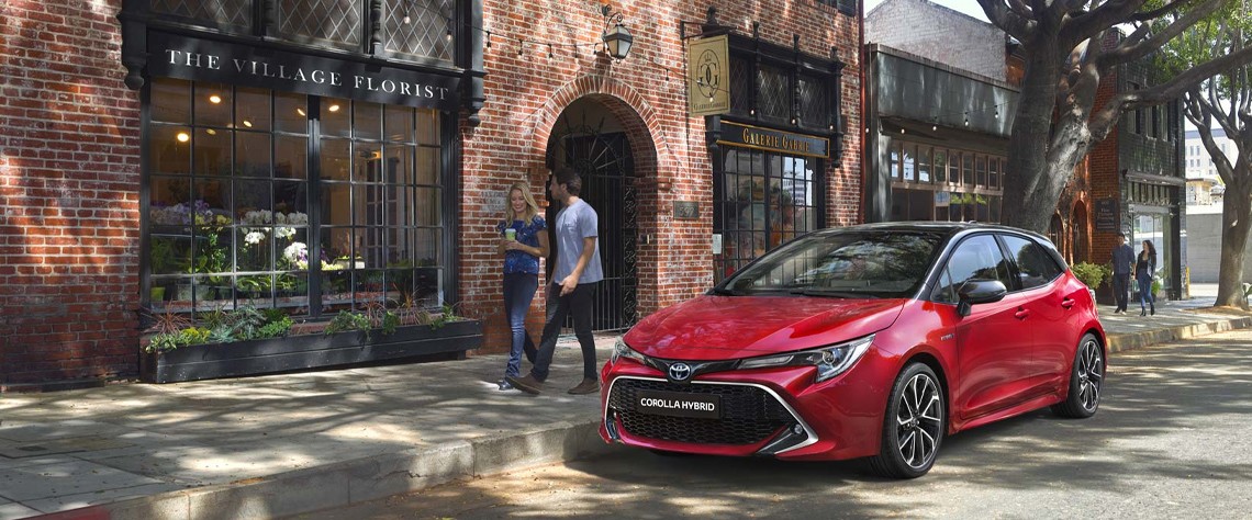 Ein Toyota Coralla Hybrid steht geparkt am Straßenrand, ein Mann und eine Frau gehen vorbei.