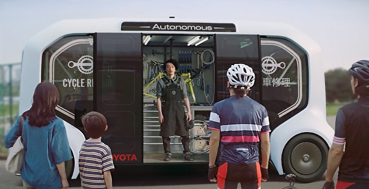 Ein Mann steht im e-Palette Konzeptfahrzeug, welches als mobile Fahrradwerkstatt verwendet wird. Davor stehen wartende Personen.