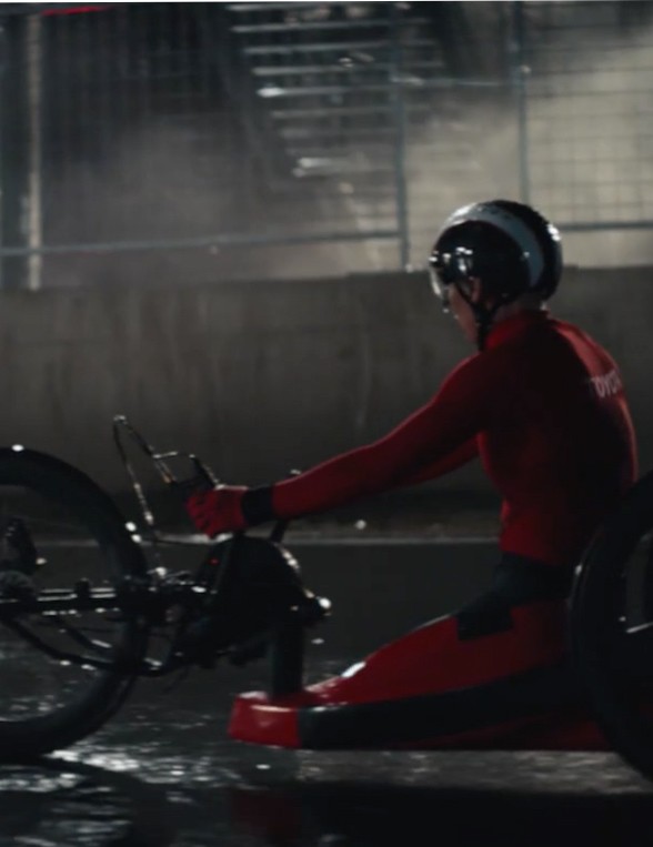 Eine Person in roter Motorsportkleidung und Helm sitzt auf dem Handbike