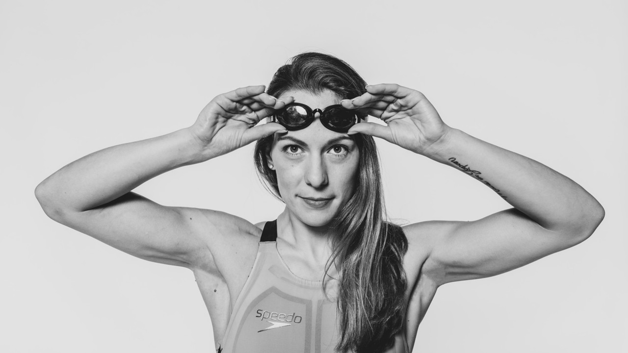 Schwarz-weiß Portrait von Maike Naomi Schwarz im Badeanzug. Sie zieht mit beiden Händen ihre Schwimmbrille auf.