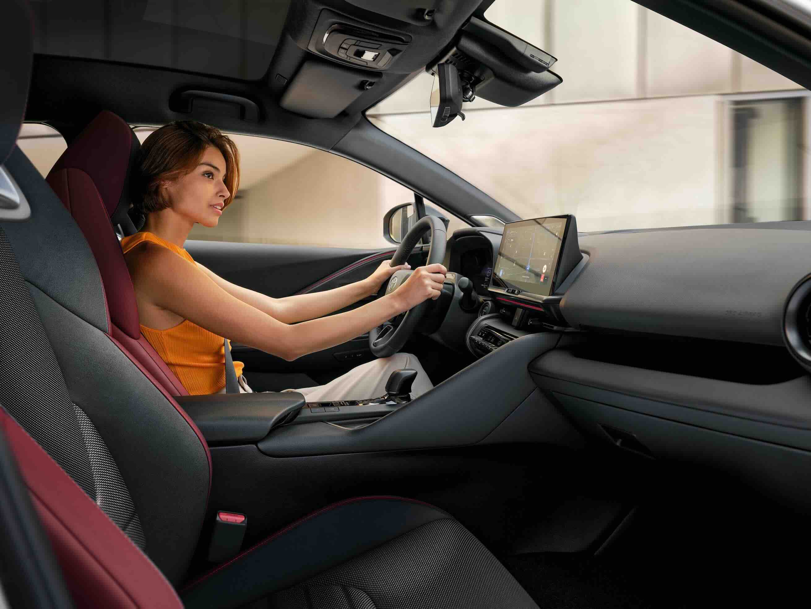 Seitliche Sicht auf eine Person am Steuer eines Toyotas, die lächelnd und konzentriert nach vorne schaut.
