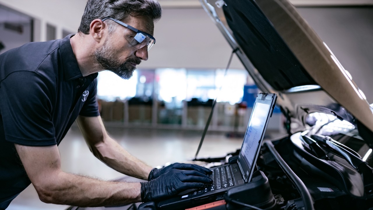 Mann mit Computer an offener Motorhaube