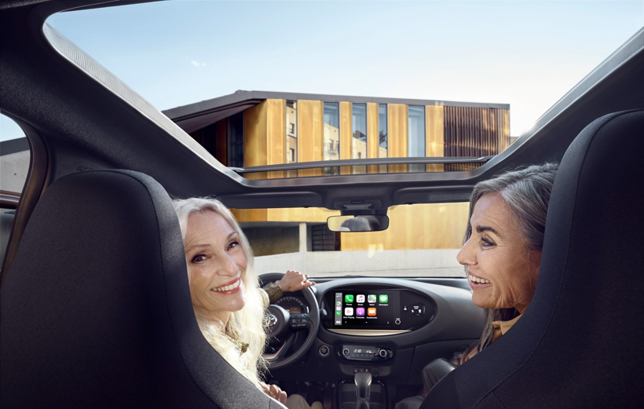 Freunde im hellen und luftigen Aygo X schauen zurück auf die Rückbank in die Kamera