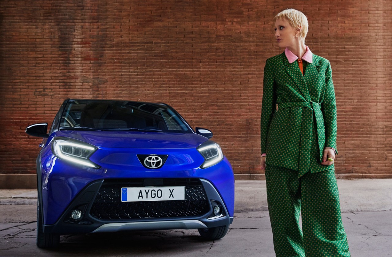 Aygo X in Juniper Blau mit Frau im Vordergrund