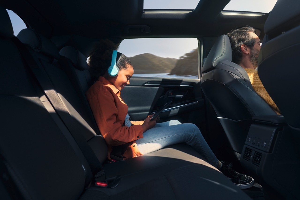 Ein Kind sitzt auf dem Rücksitz des Toyota bZ4X und hört Musik, während durch dem Seitenfenster Berge zu sehen sind.