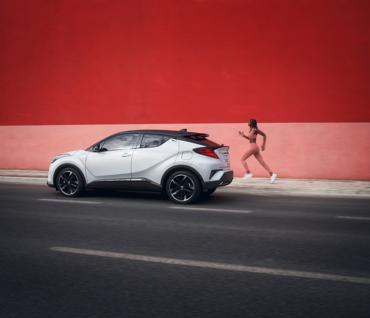 Toyota C-HR mit Joggerin vor bunter Mauer